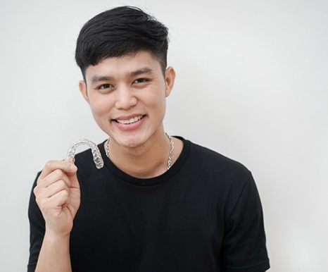 young man smiling and holding Invisalign clear braces in Spring, TX