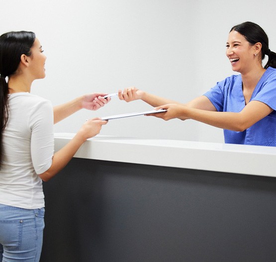 Smiling dental assistant handing patient form