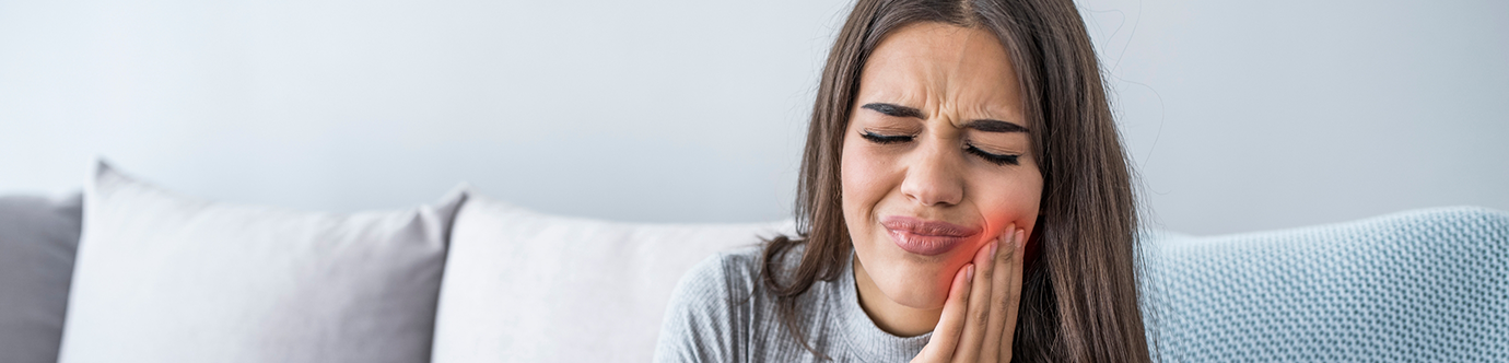 Woman holding her cheek in pain before seeing an emergency dentist in Spring