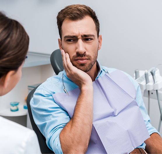 Man holding his cheek in pain while talking to his dentist