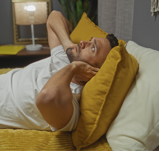 Man covering his ears while laying awake in bed