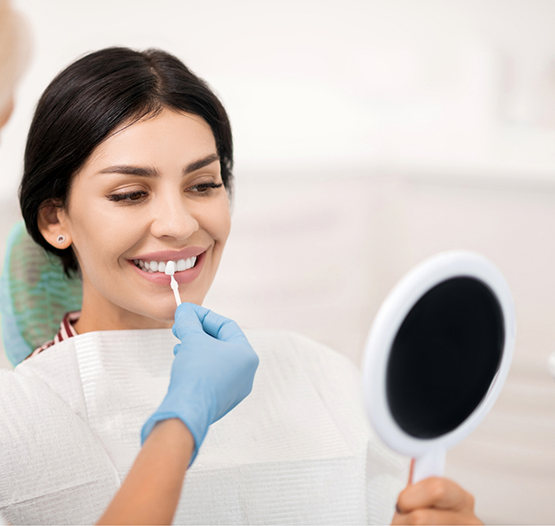 Woman smiling as a dentist holds a veneer in front of her tooth