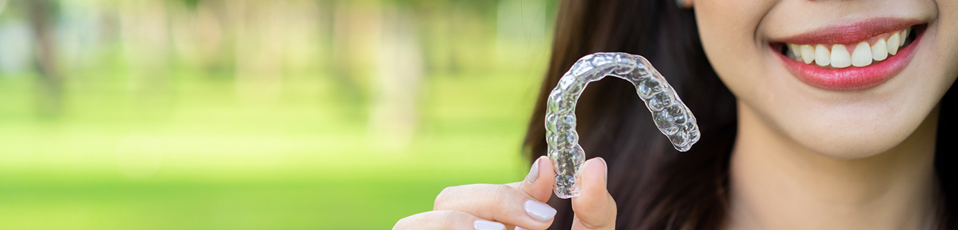 Smiling woman holding an Invisalign clear aligner in Spring