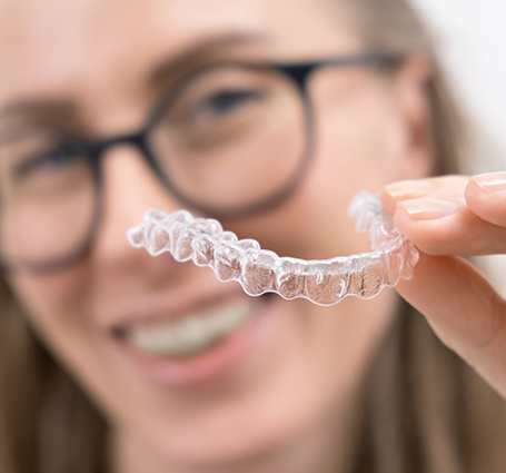 Smiling young woman with glasses holding Invisalign