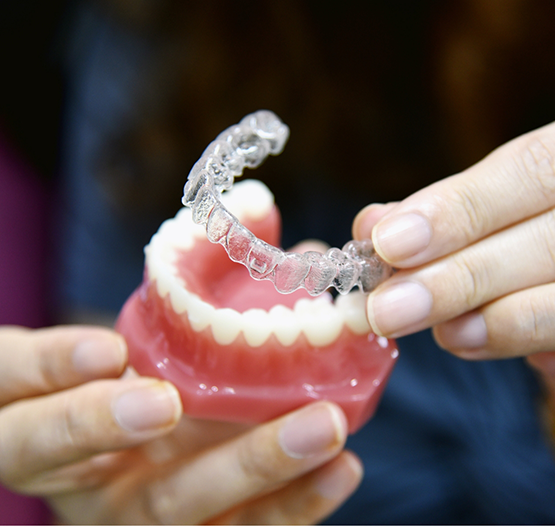Dentist placing an Invisalign aligner over a model of teeth