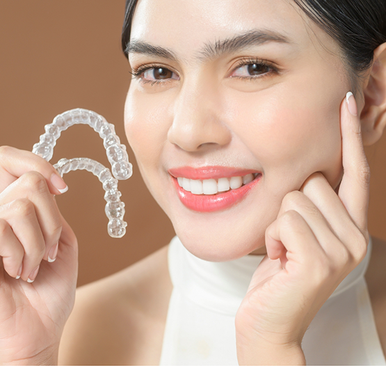 Smiling woman touching her face and holding Invisalign aligners