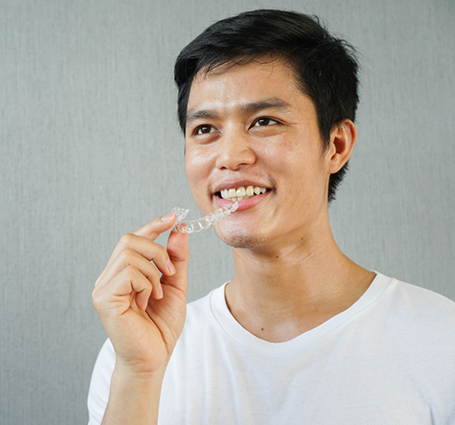 Smiling man holding an Invisalign tray near his mouth