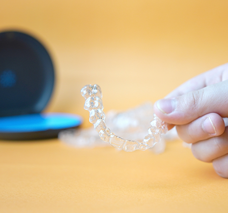 Hand holding a clear aligner over its storage case
