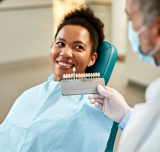 Woman smiling while her dentist holds a row of veneers