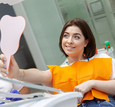 Young woman in the dental chair looking at her teeth in a mirror